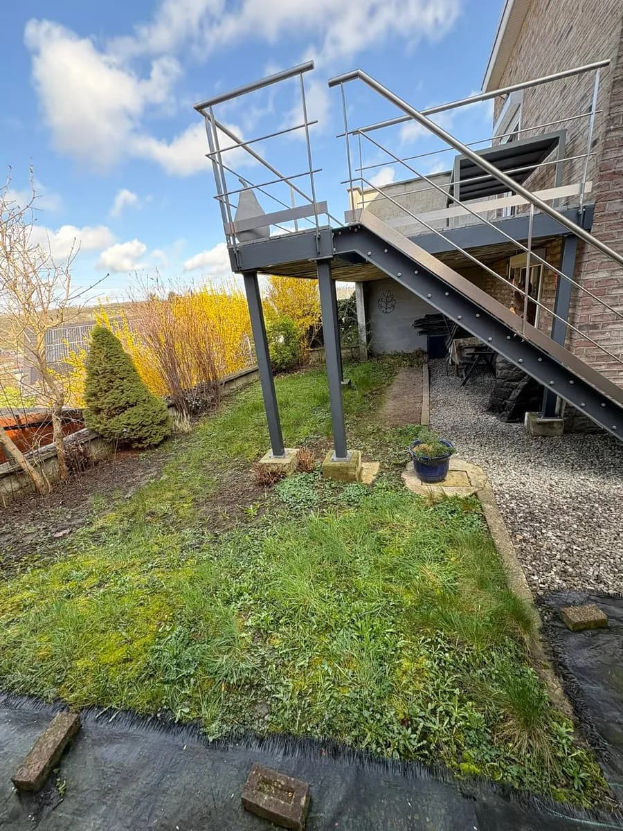 Zone envahie d’herbes folles sous la terrasse avant aménagement